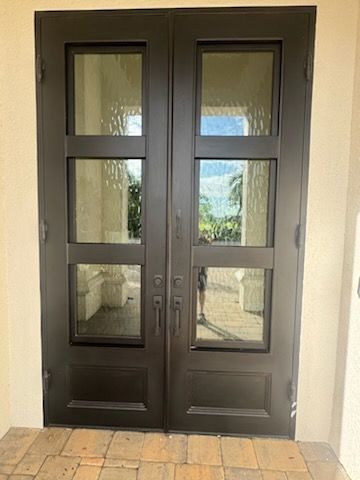 Wooden double doors with arched tops, ornate black ironwork, set in a stone wall.