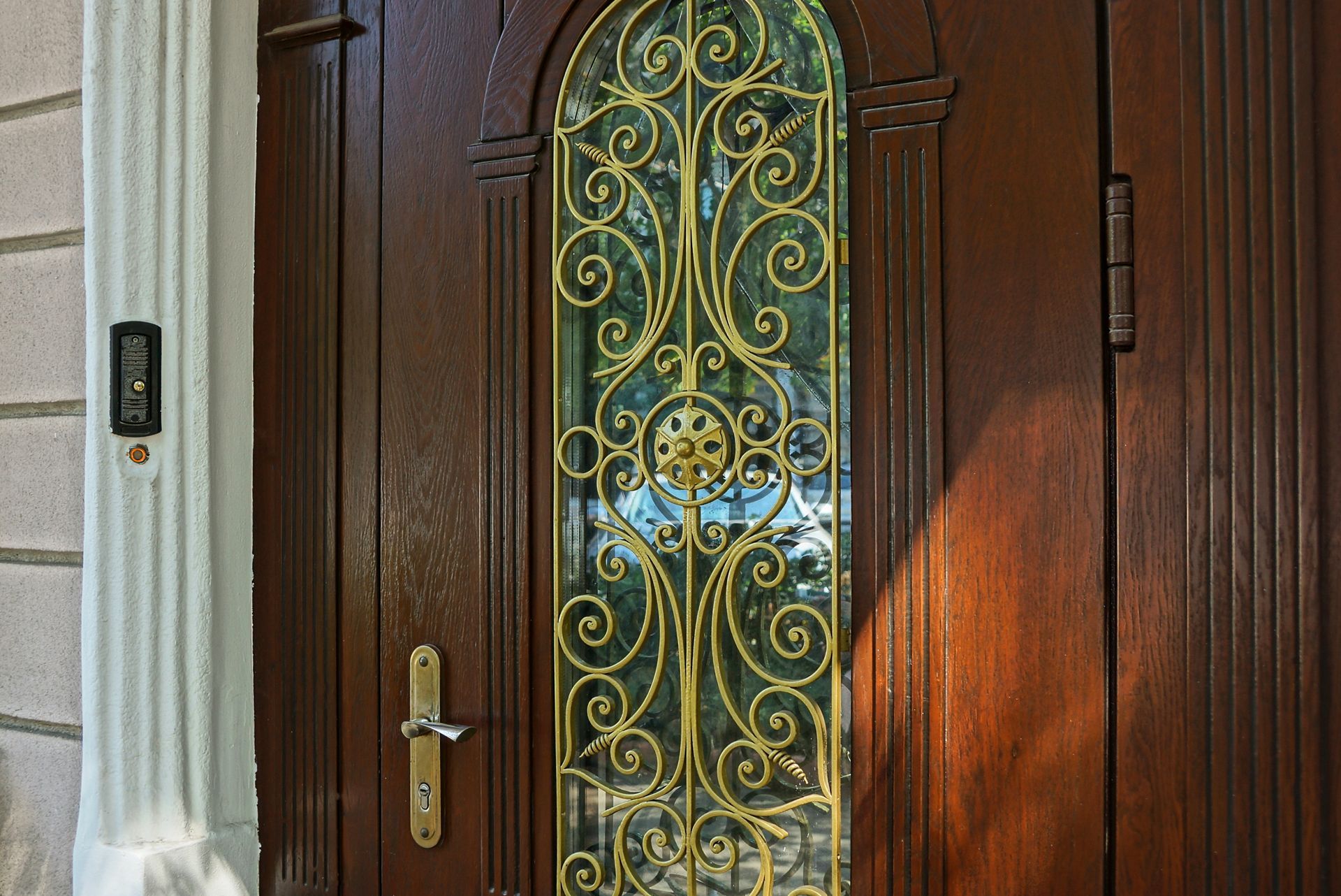 Brown wooden door with gold ornate window, next to a white pillar.