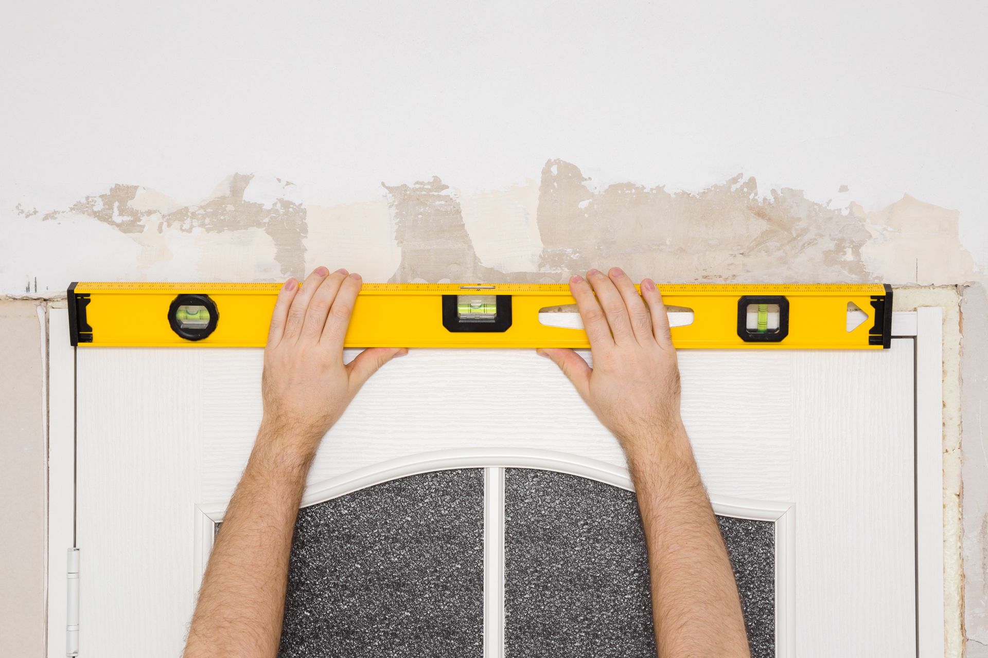 Person using a yellow level above a door to check if it's straight, indoors.