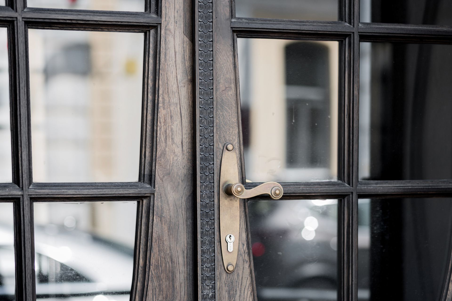 Close-up of a weathered, wooden door with glass panes and an antique brass handle.