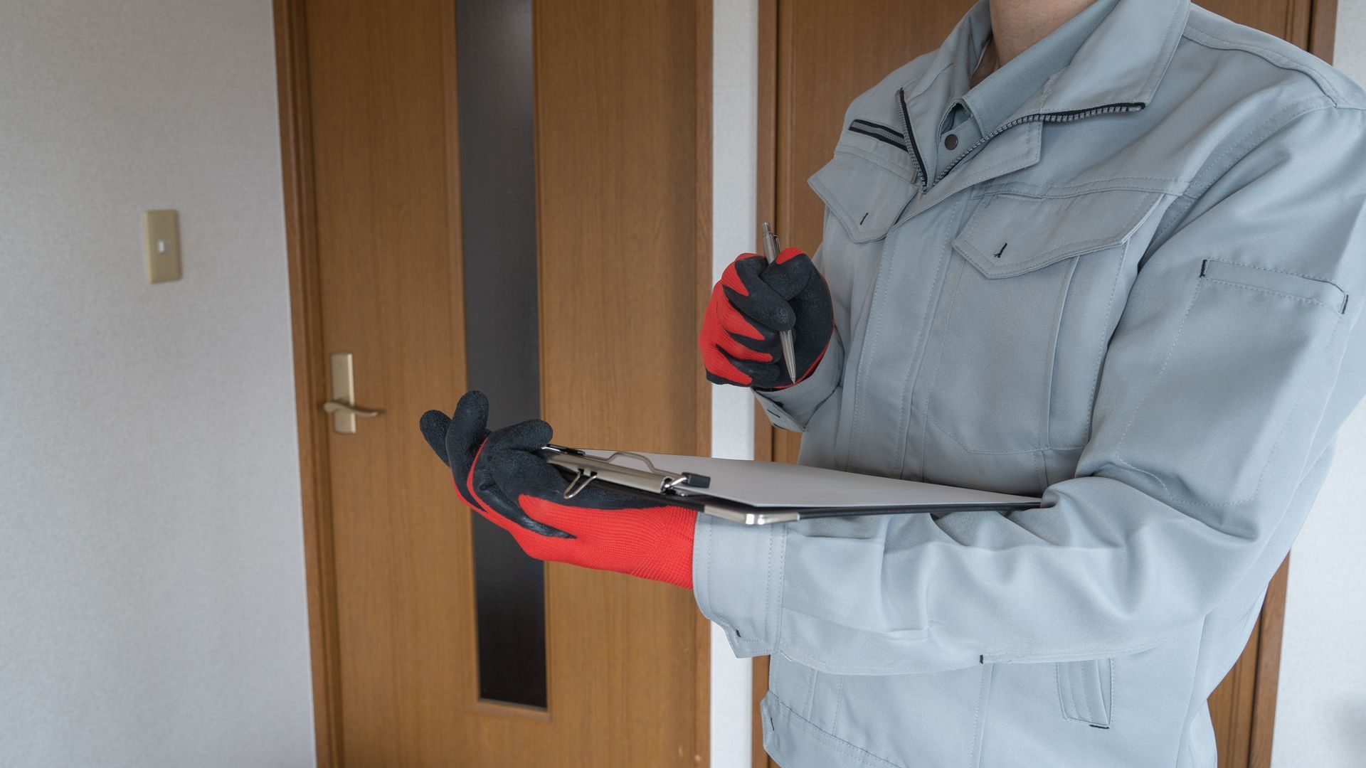 Person in work uniform holding clipboard and pen near a closed door.