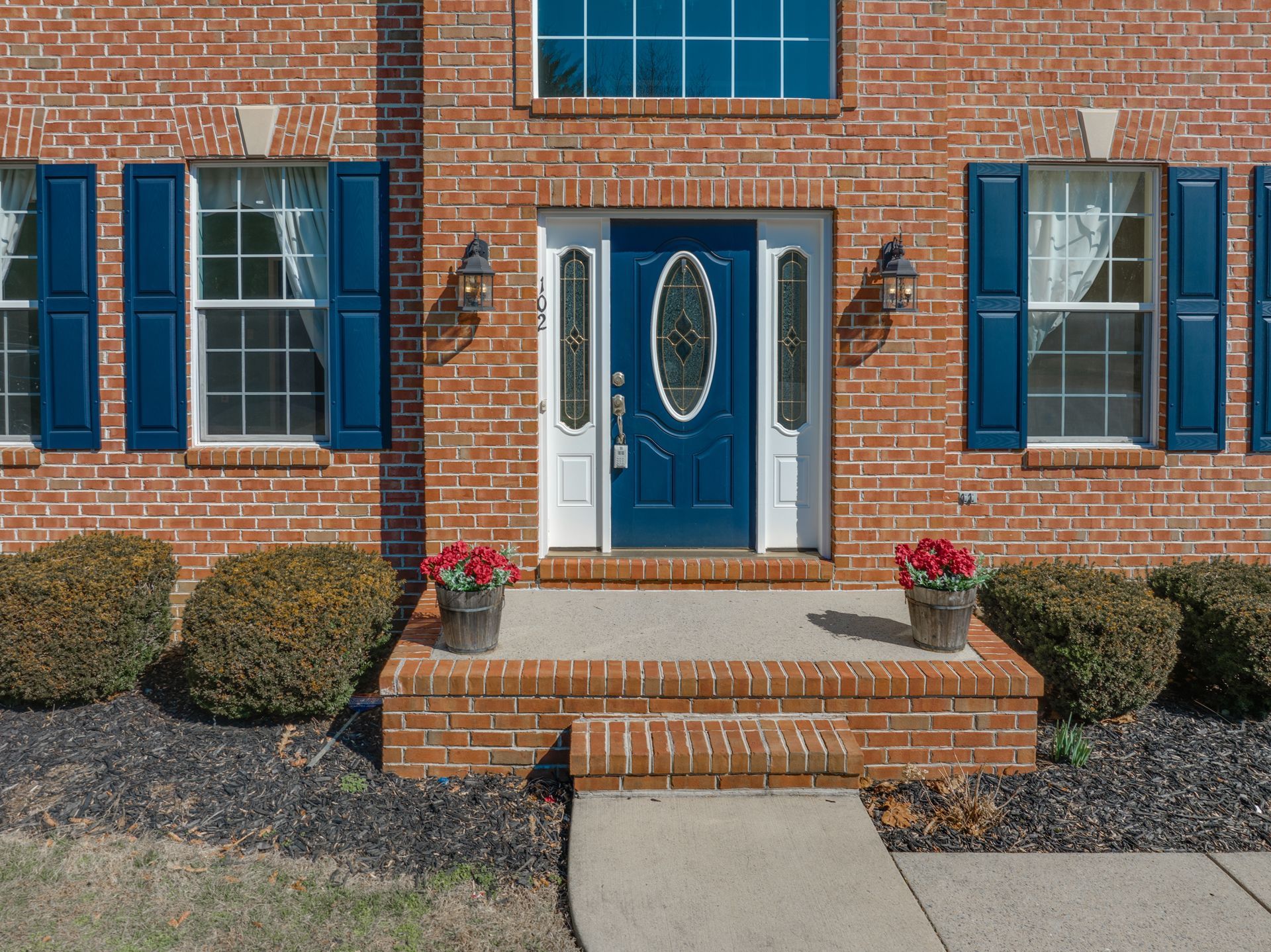Brick house with a blue front door, matching shutters, and two flower pots on the porch.
