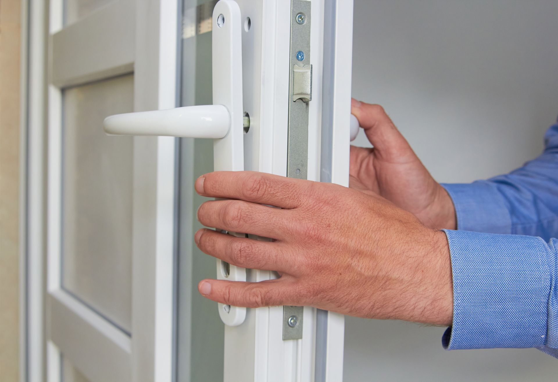 Person's hands manipulating a white door handle and latch on a white door.