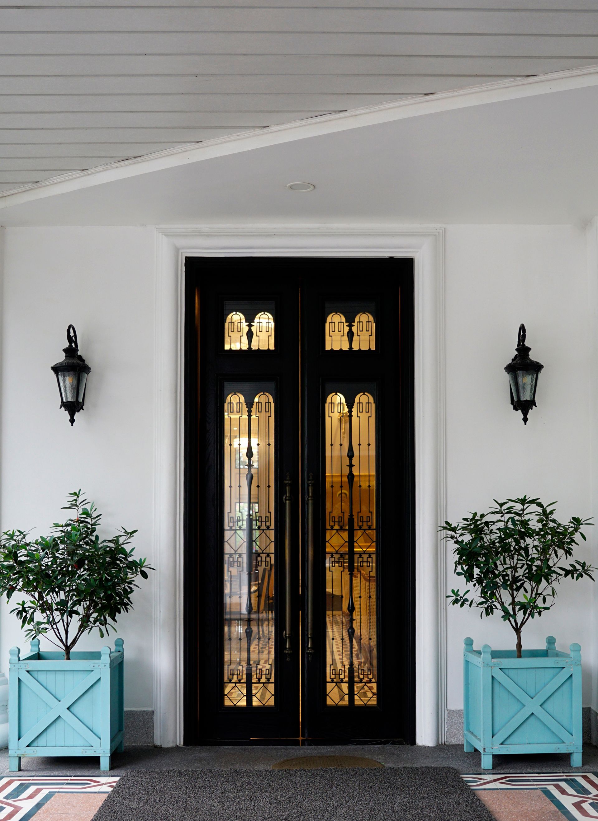 Black double doors with decorative glass panels flanked by teal planters and black lanterns.