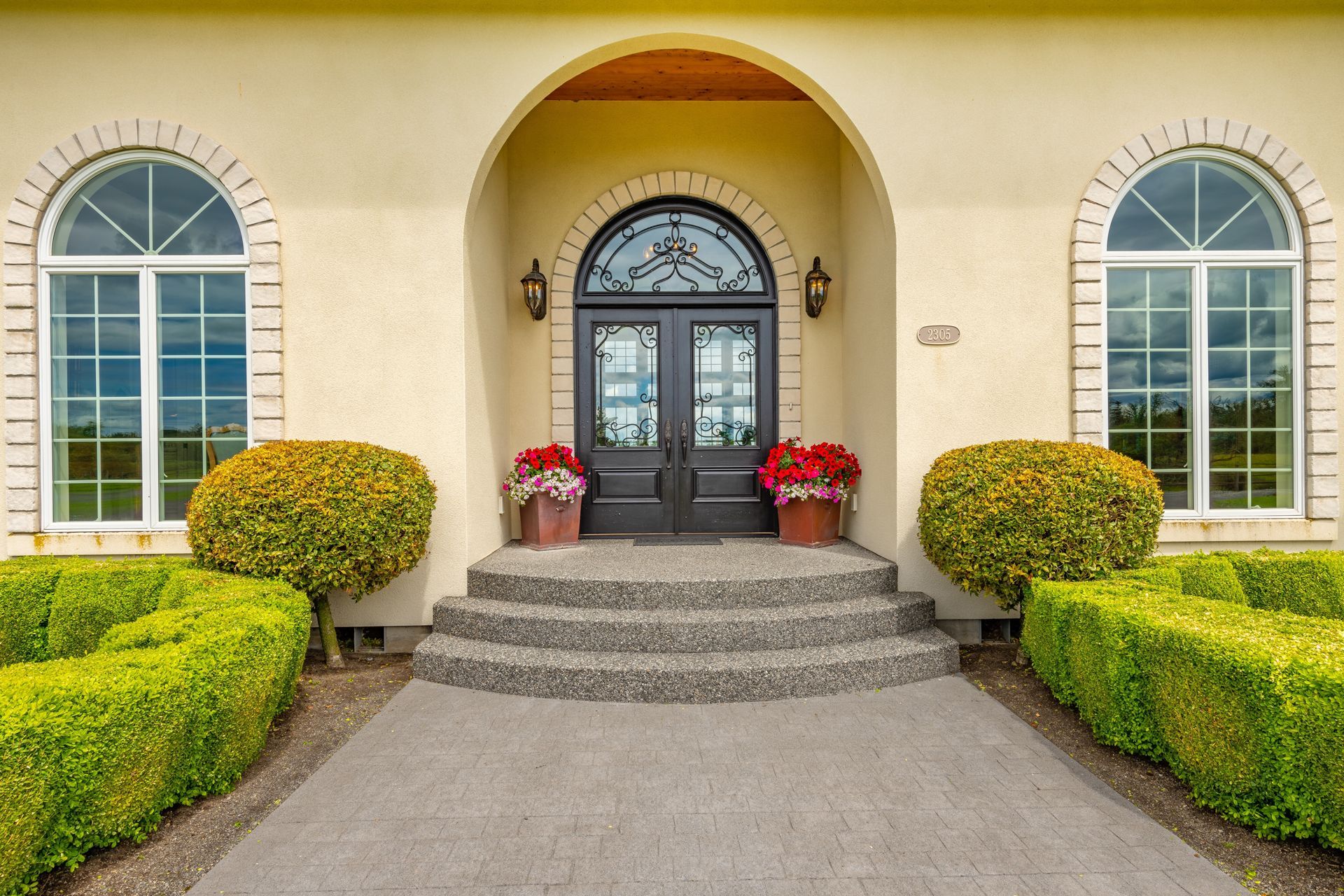 Beige house entrance with arched doorway, black double doors, and symmetrical windows.