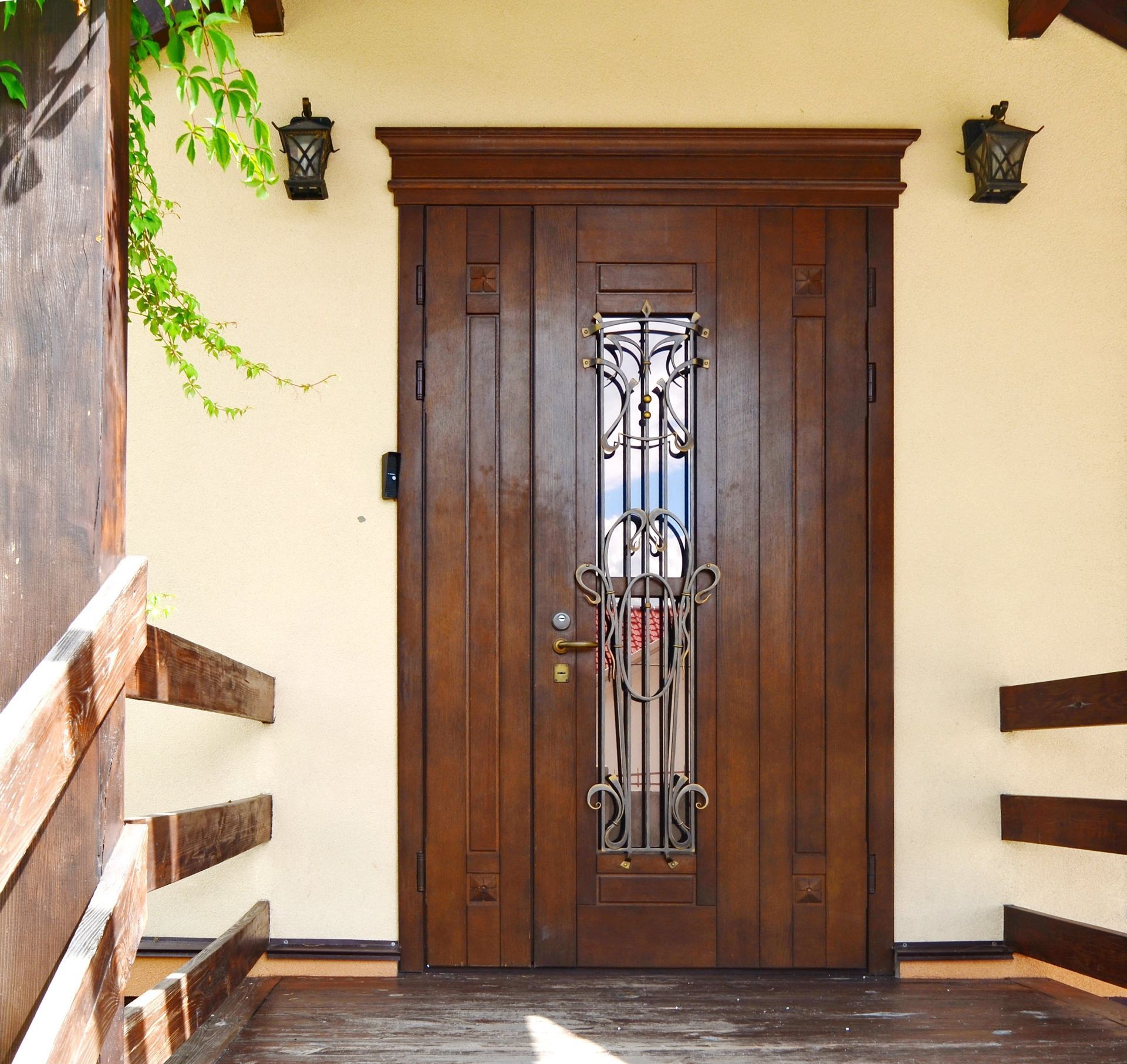 Brown wooden front door with ornate metal window, on a tan building exterior with a porch.