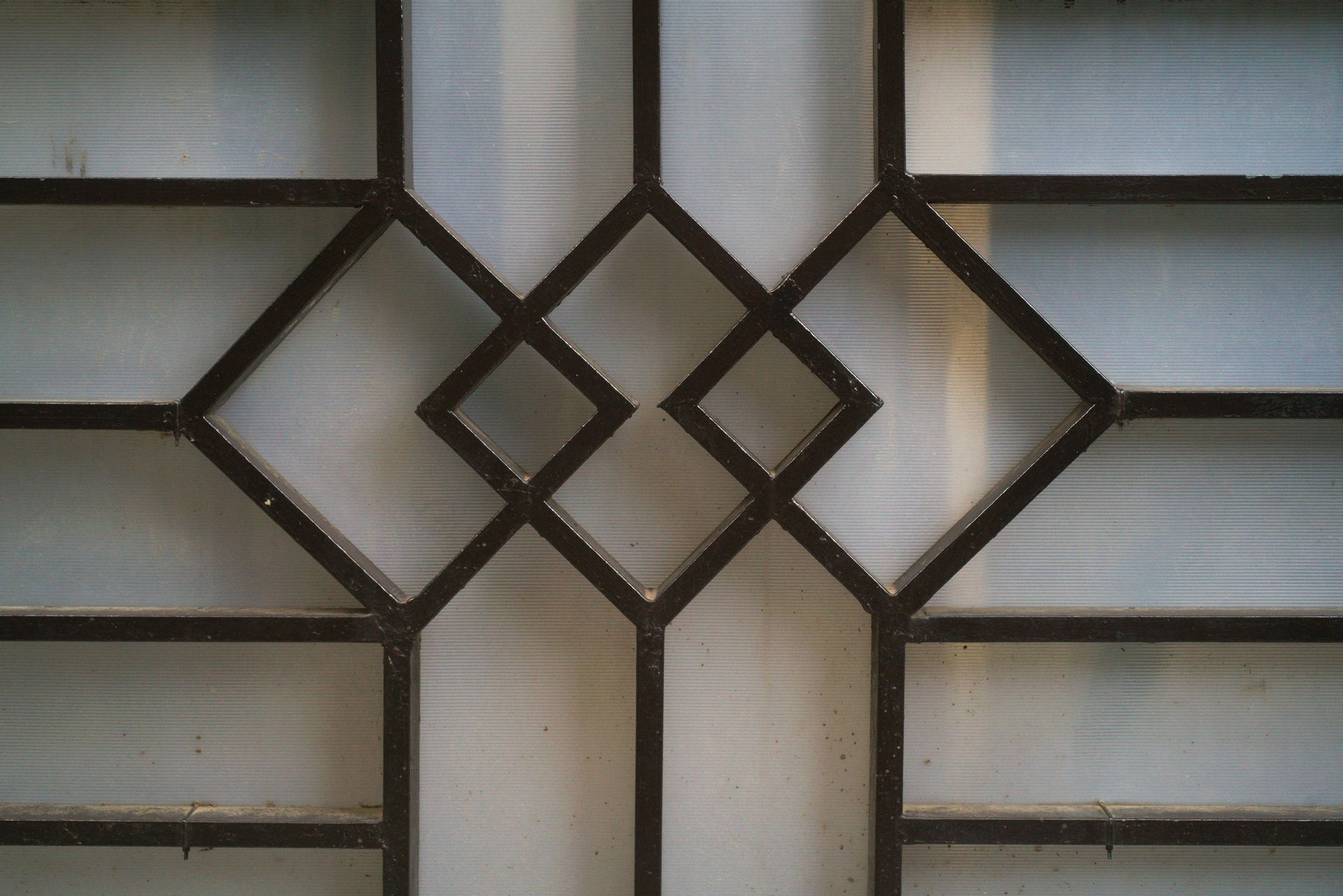 Dark metal window frame with geometric diamond design, frosted glass.