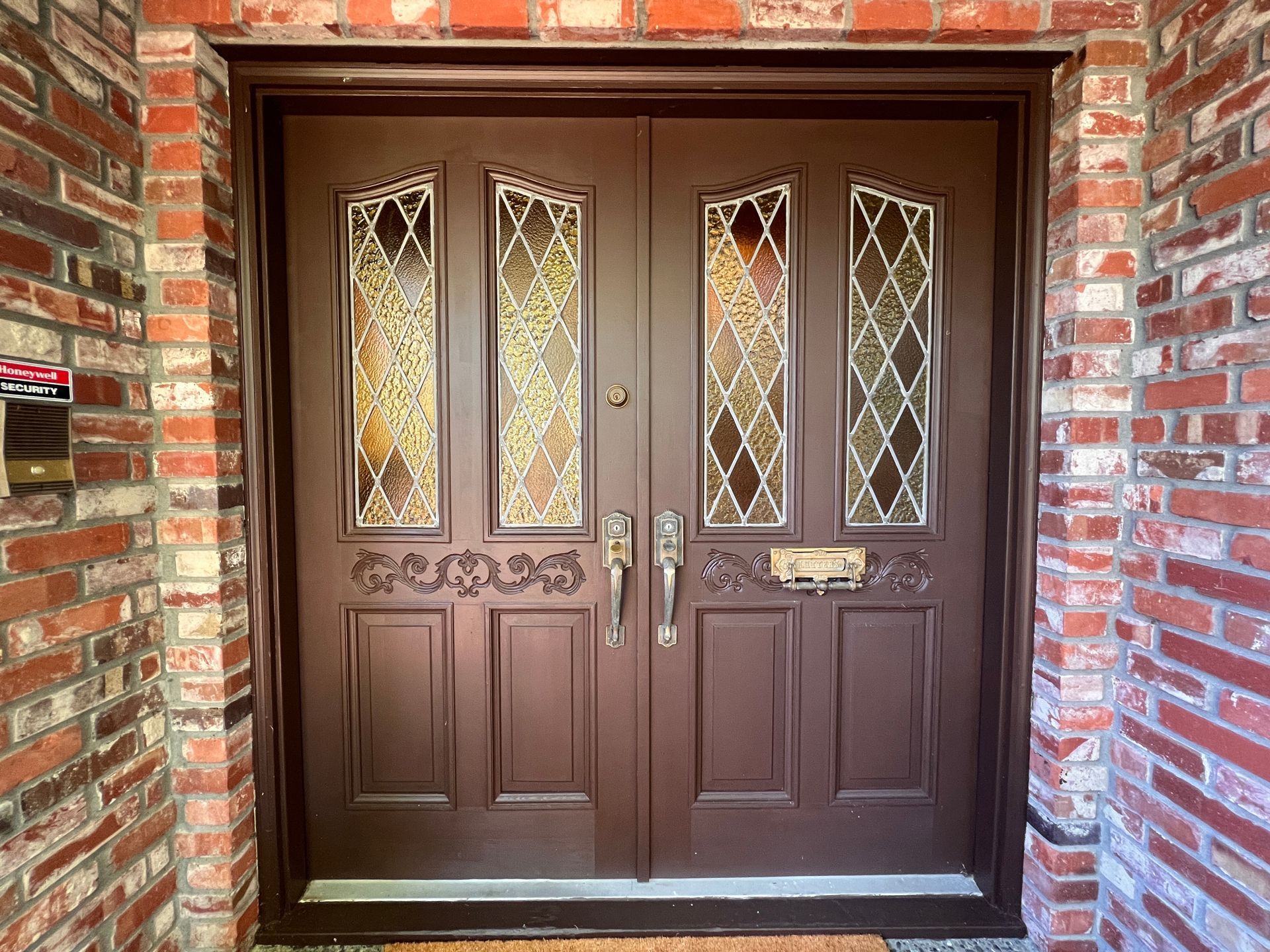 Brown double doors with stained glass panels, set in brick.
