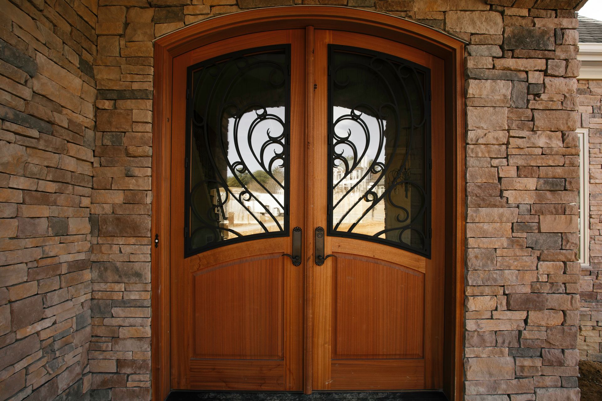 Wooden double doors with arched tops, ornate black ironwork, set in a stone wall.