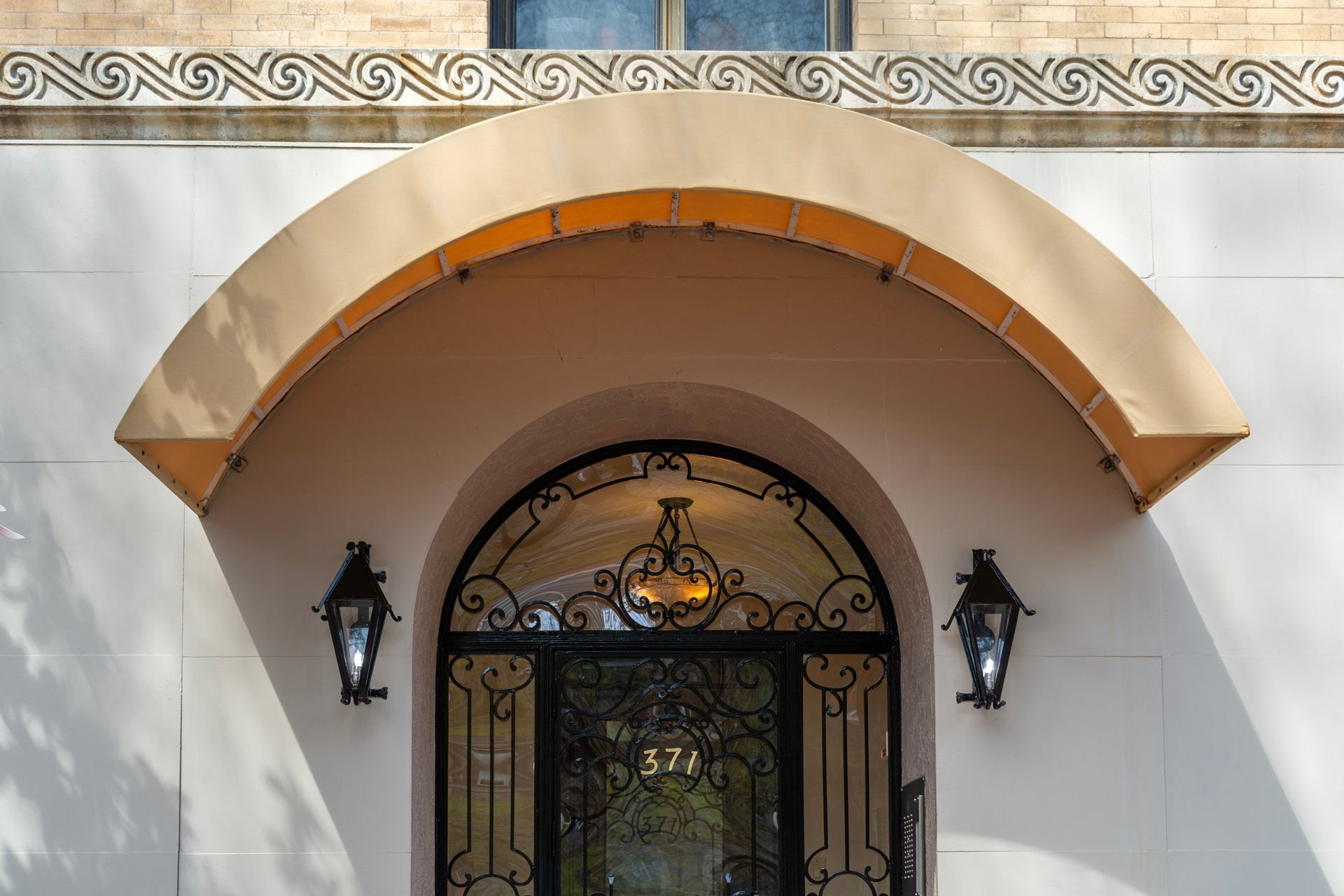 Arched doorway with a tan awning and ornate black metal door.