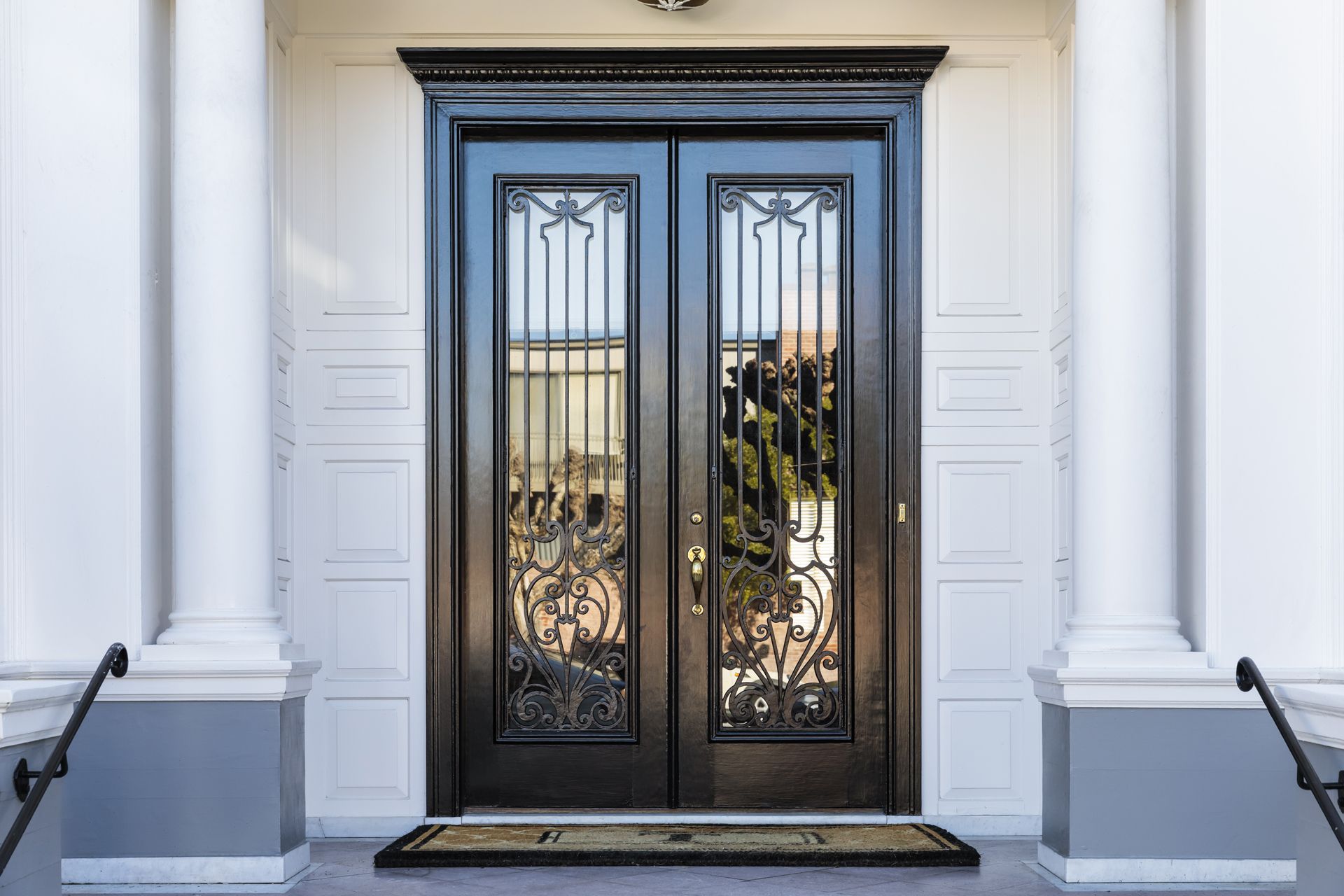 Black double doors with decorative ironwork, flanked by white columns, on a porch.
