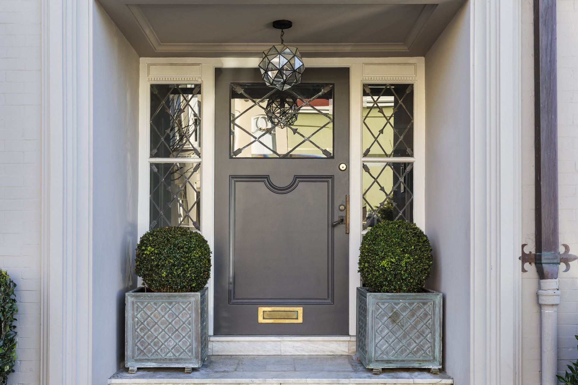 Gray front door with sidelights, hanging light, and potted topiaries.