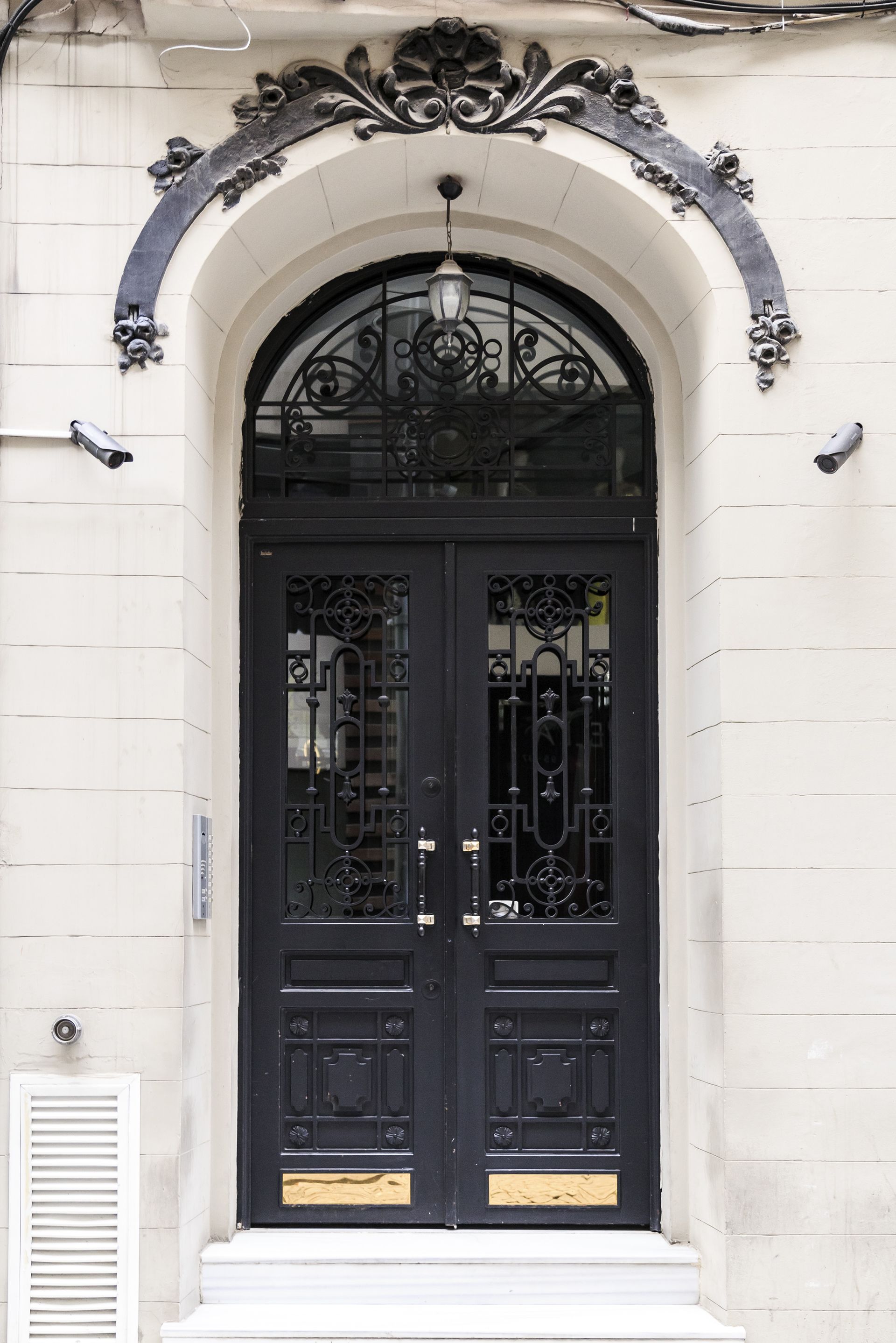 Black ornate double doors beneath an arched transom window and decorative lintel.