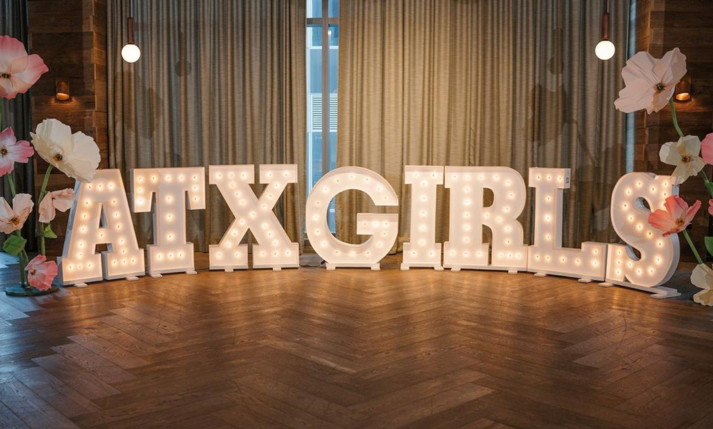 The word atxgirls is written in lights on a wooden floor.