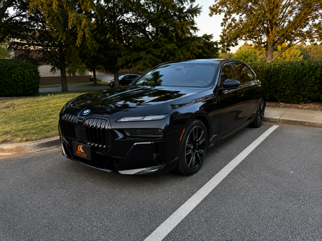Black BMW sedan parked outdoors in a lot, with trees and hedges in the background.