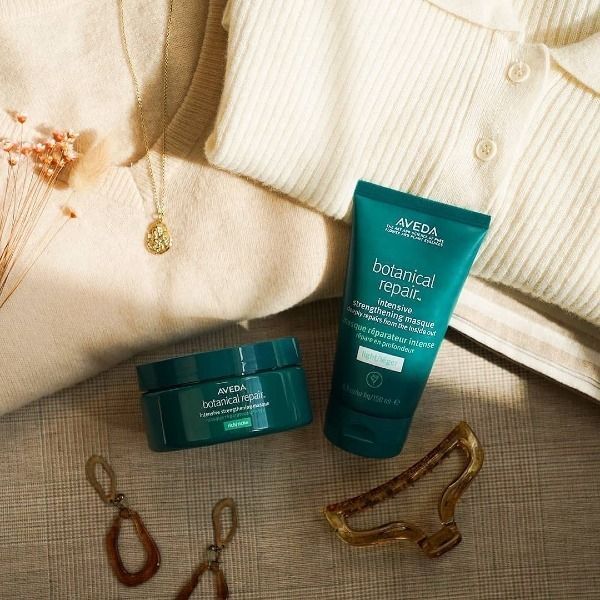 Spa treatment with towels, leaves, loofahs, oil, brush, candle, and stones on white.