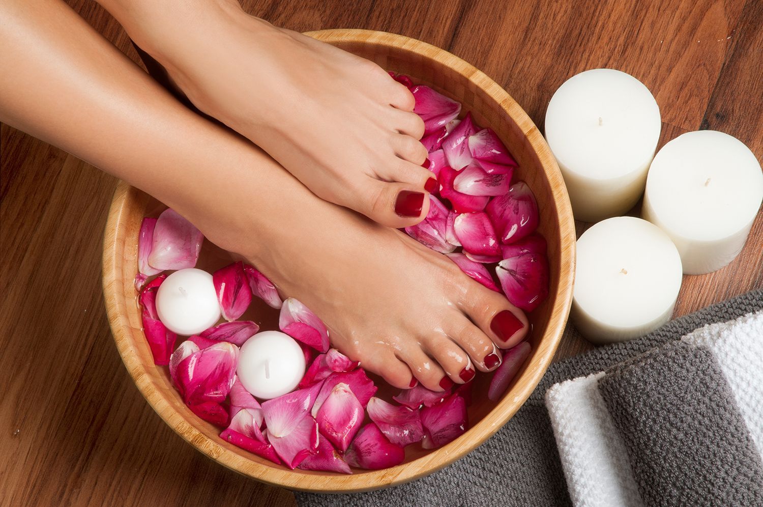 Feet soaking in a wooden bowl filled with rose petals and candles for a spa treatment.