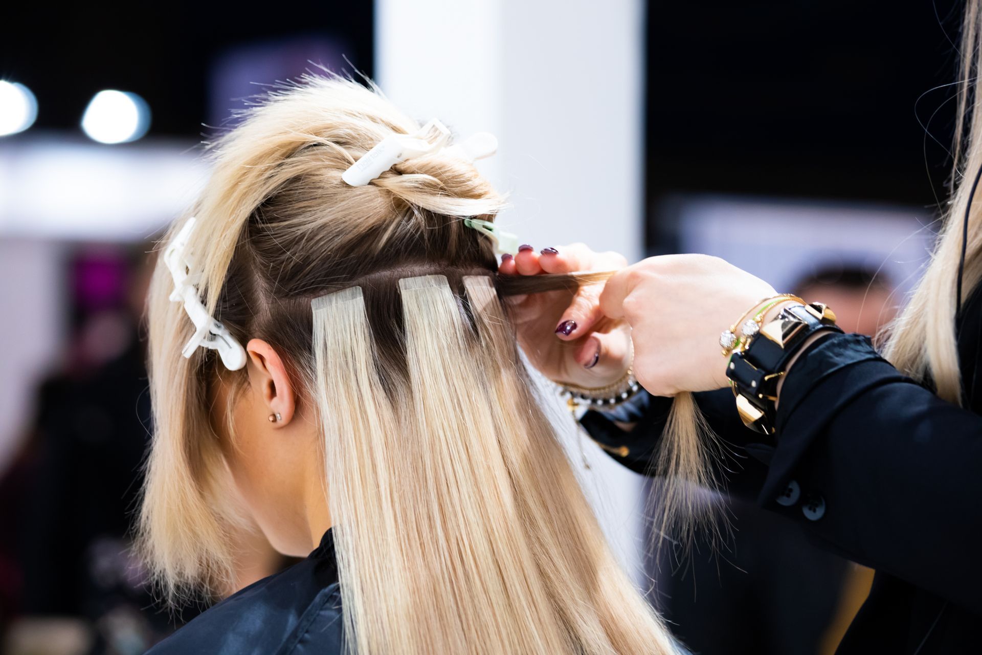 Stylist applying hair extensions to blonde hair in a salon setting. Stylist applying hair extensions to blonde hair in a salon setting.