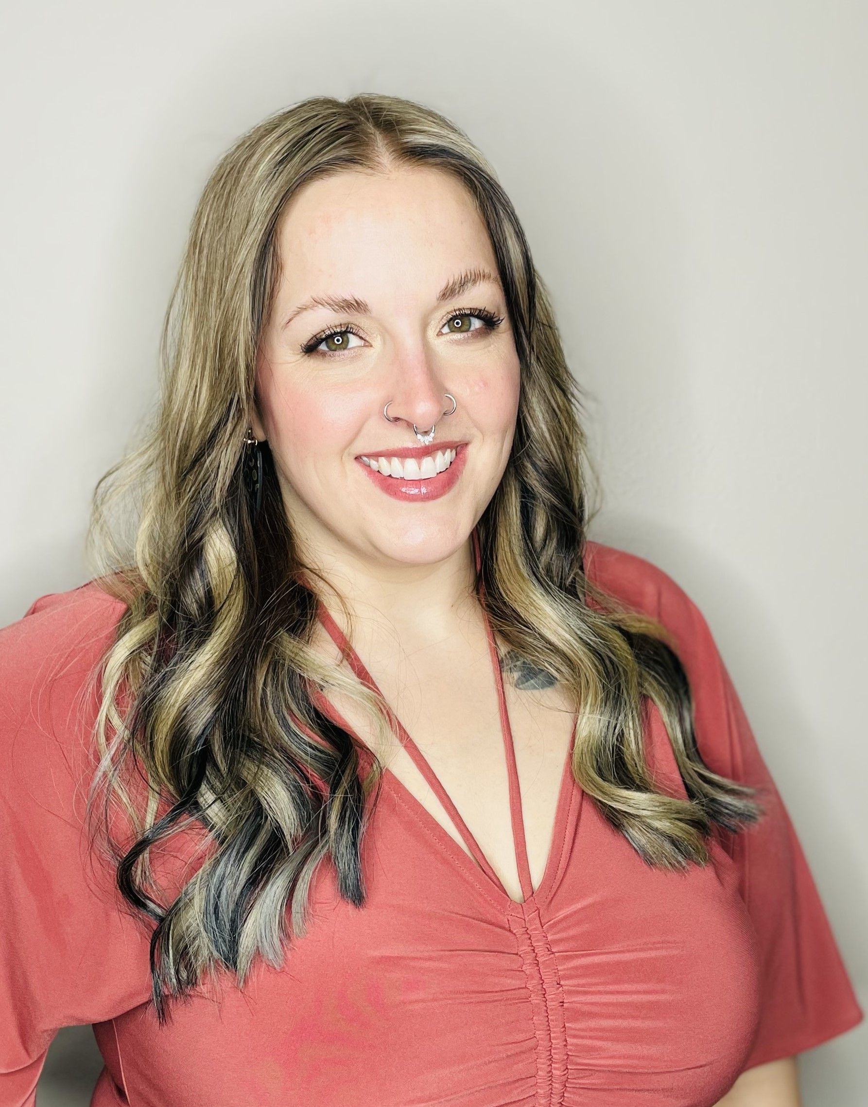 Woman with highlighted hair smiles, wearing a rust-colored top.