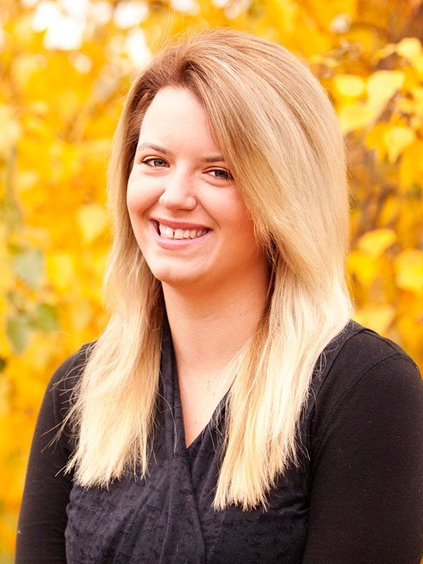 Woman with blonde hair smiles against a backdrop of yellow autumn leaves.