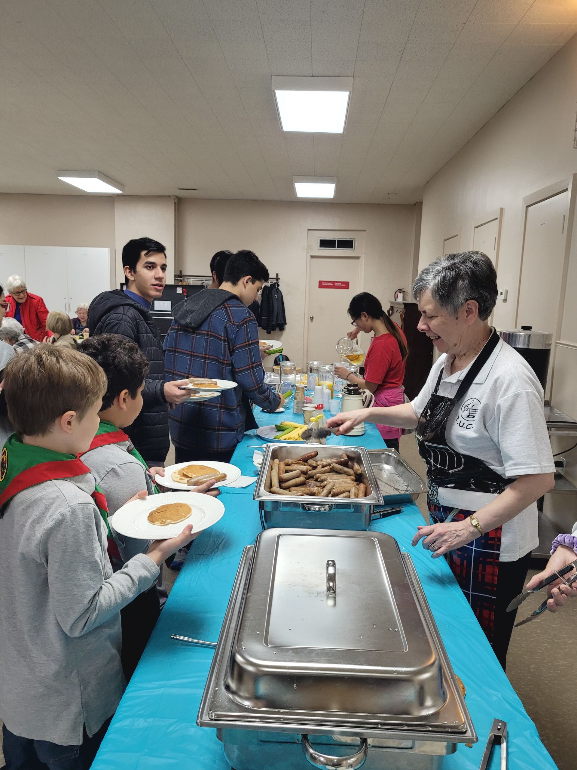 a group of people are standing around a table eating food .