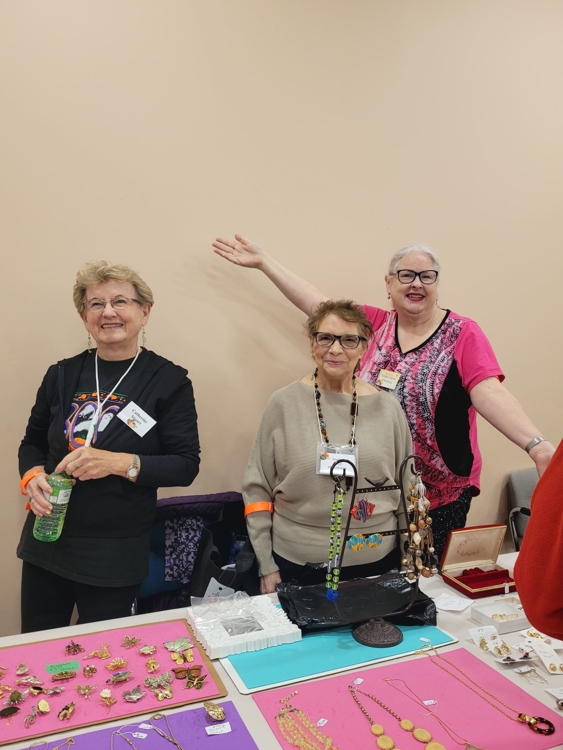 three women are standing around a table with jewelry on it .