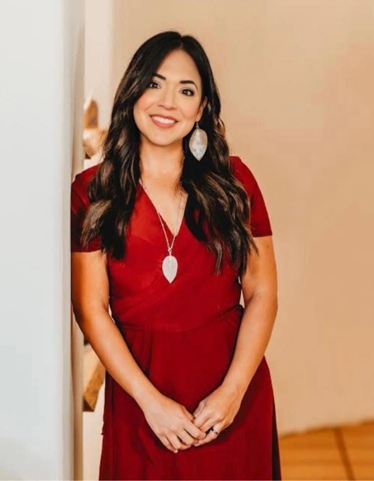 A woman is sitting at a desk with a laptop and a vase of flowers.