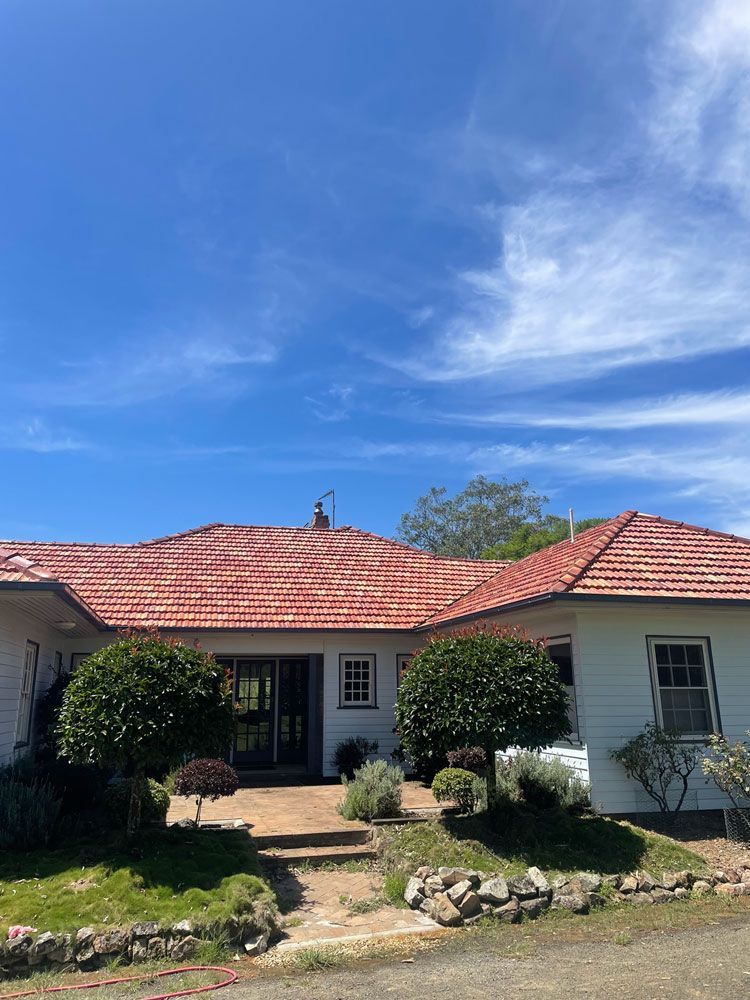 A White House With A Red Tile Roof And A Blue Sky In The Background — Bulley Roof Restoration, Painting & Pressure Cleaning in Gloucester, NSW