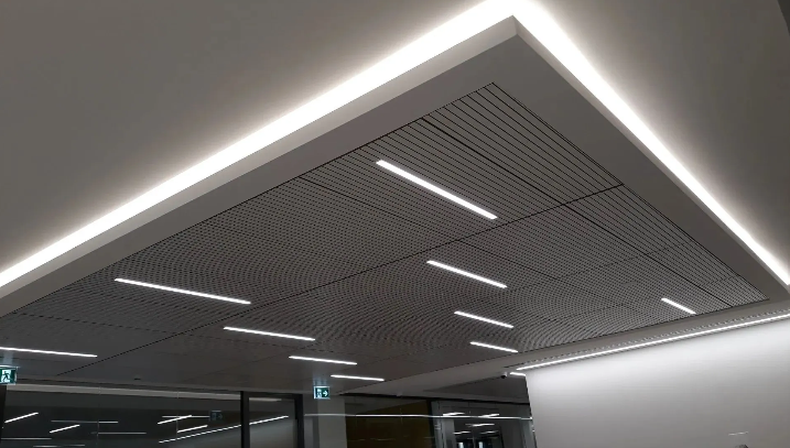 Controsoffitto bianco con illuminazione integrata, a incasso e lineare. Pannelli forati con motivo a onde.