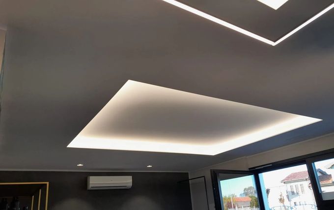 Soffitto moderno con apparecchi di illuminazione quadrati da incasso, insieme a uno rettangolare e pareti scure.
