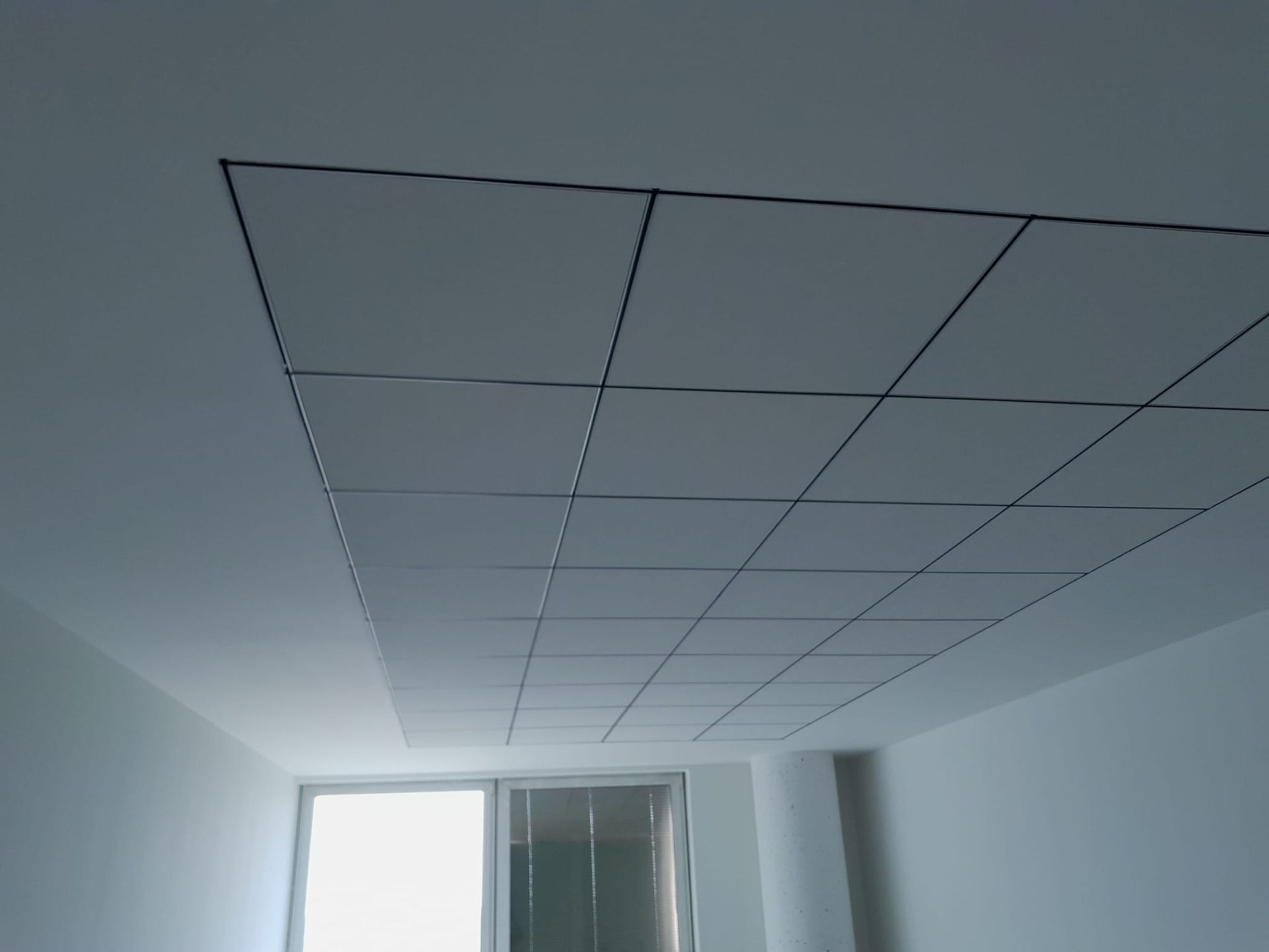 Soffitto bianco con griglia incassata di pannelli quadrati, possibilmente per l'illuminazione o l'accesso.