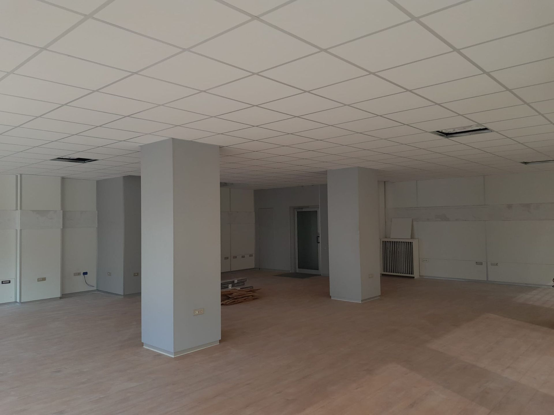 Stanza vuota con soffitto bianco, colonne di sostegno e pareti grezze.