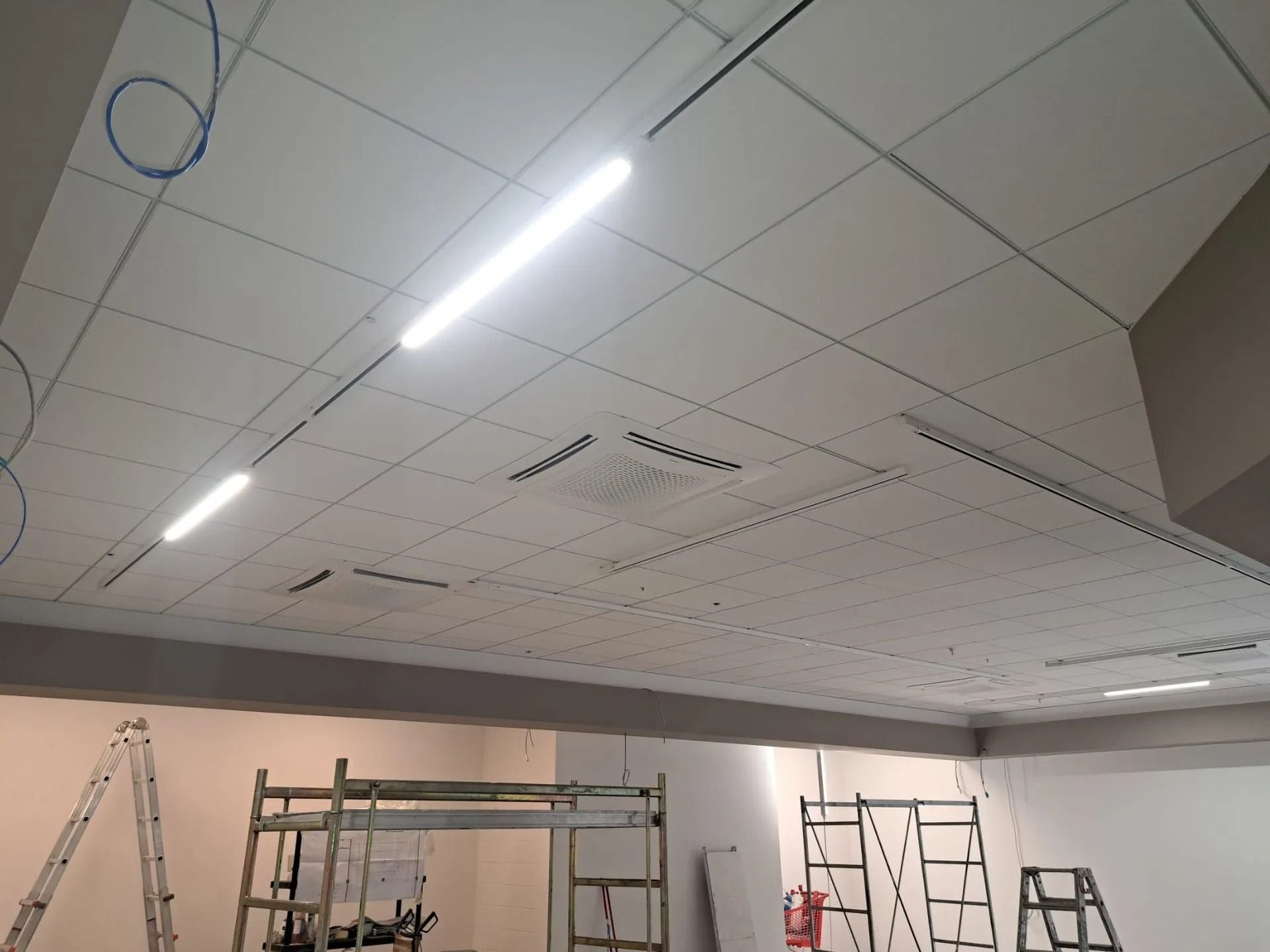 Controsoffitto con piastrelle bianche, due luci fluorescenti e una stanza parzialmente costruita con scale.