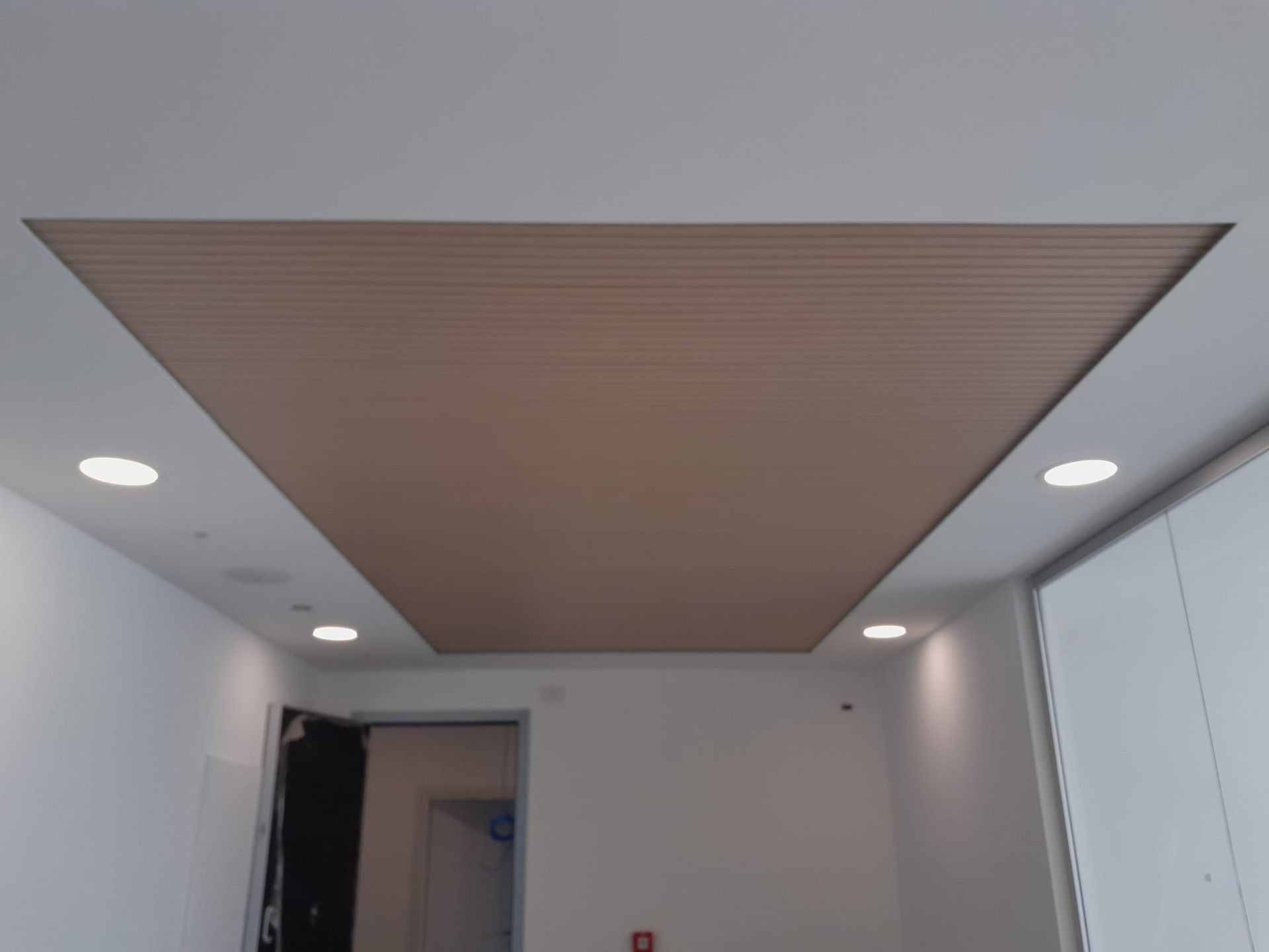 Soffitto con pannello in legno incassato, circondato da pareti bianche e luci incassate.