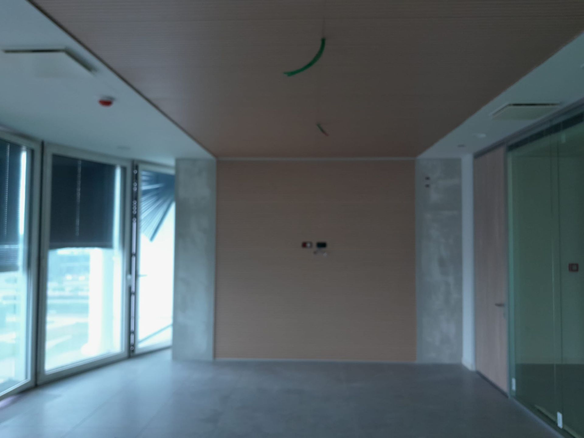 Stanza vuota con grandi finestre, pareti e soffitto color cuoio, pavimento grigio.