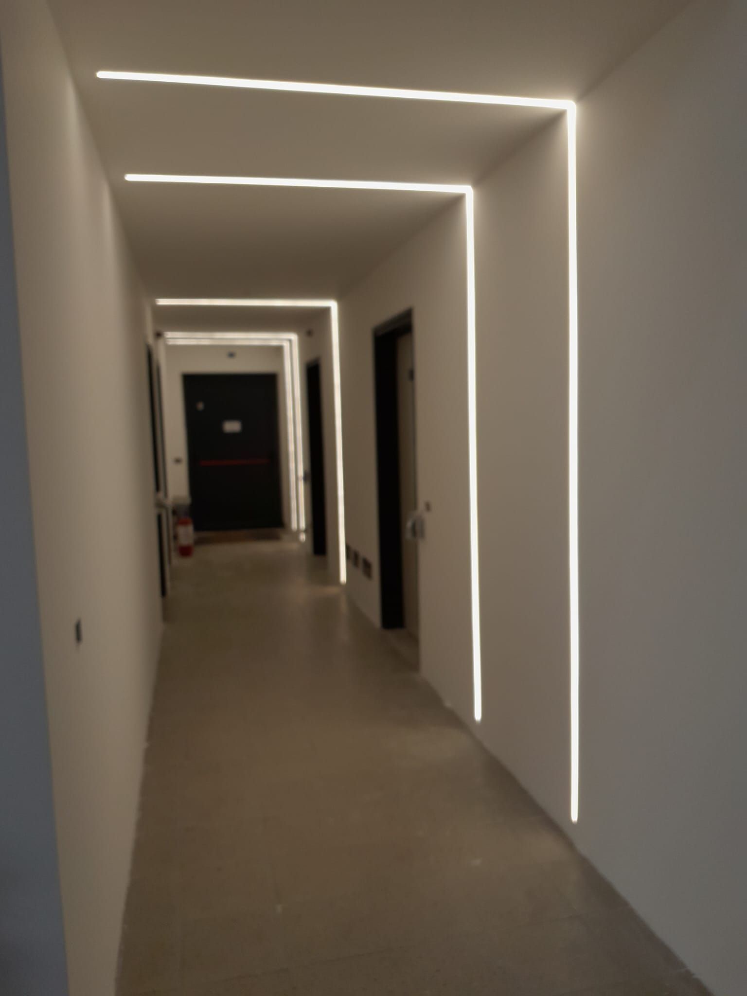 Un lungo corridoio con luci LED lineari incassate sul soffitto e sulle pareti. Le porte fiancheggiano i lati.