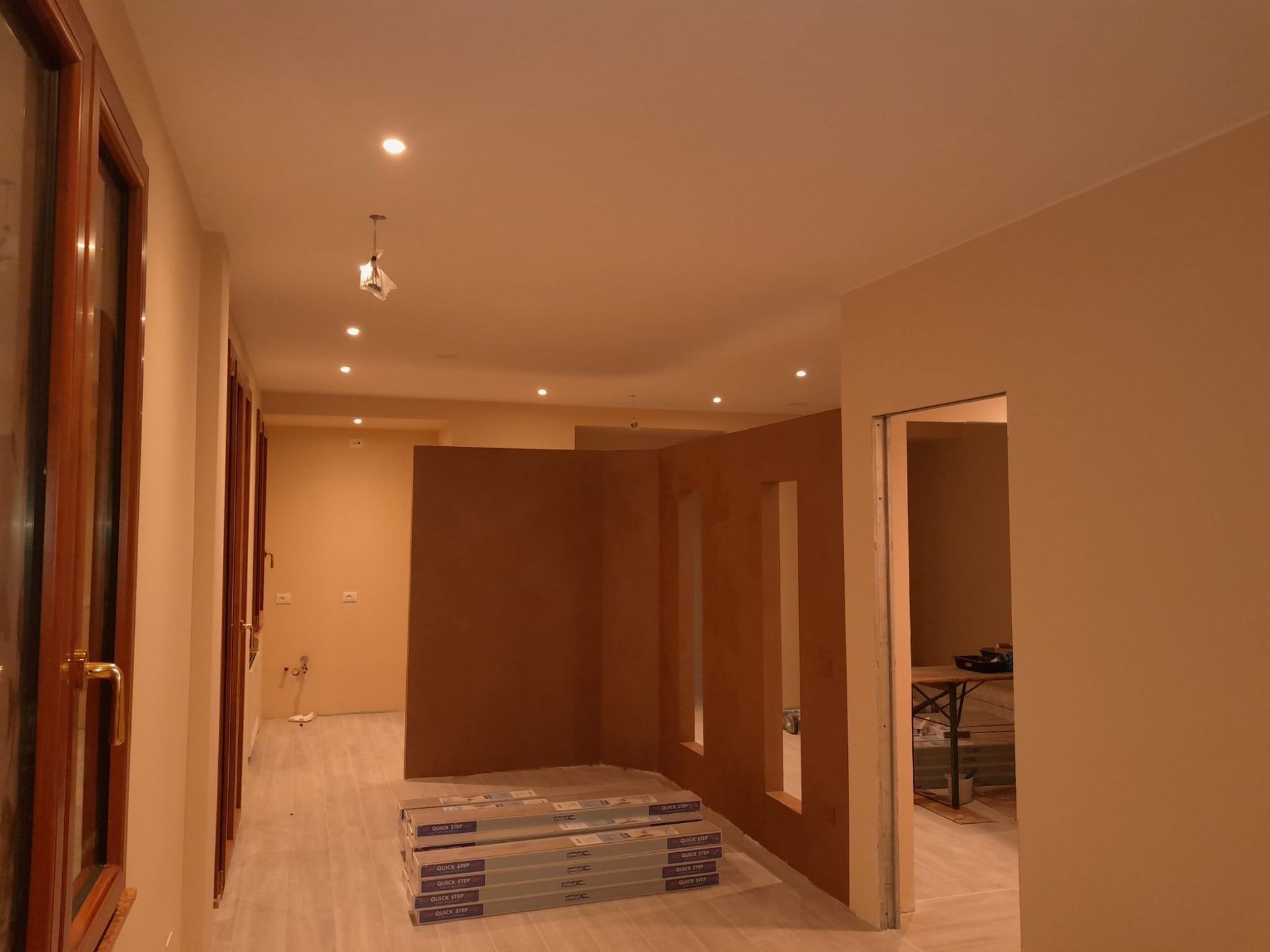 Corridoio in costruzione con luci da incasso, pareti grezze e porta.