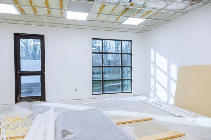 Interno di una stanza in costruzione con pareti bianche, finestre e soffitto a vista.