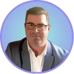 Man wearing glasses, white shirt, and a blue blazer, set against a blue background.