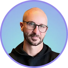 Man with glasses and bald head, smiling, in front of a blue gradient background, wearing black.