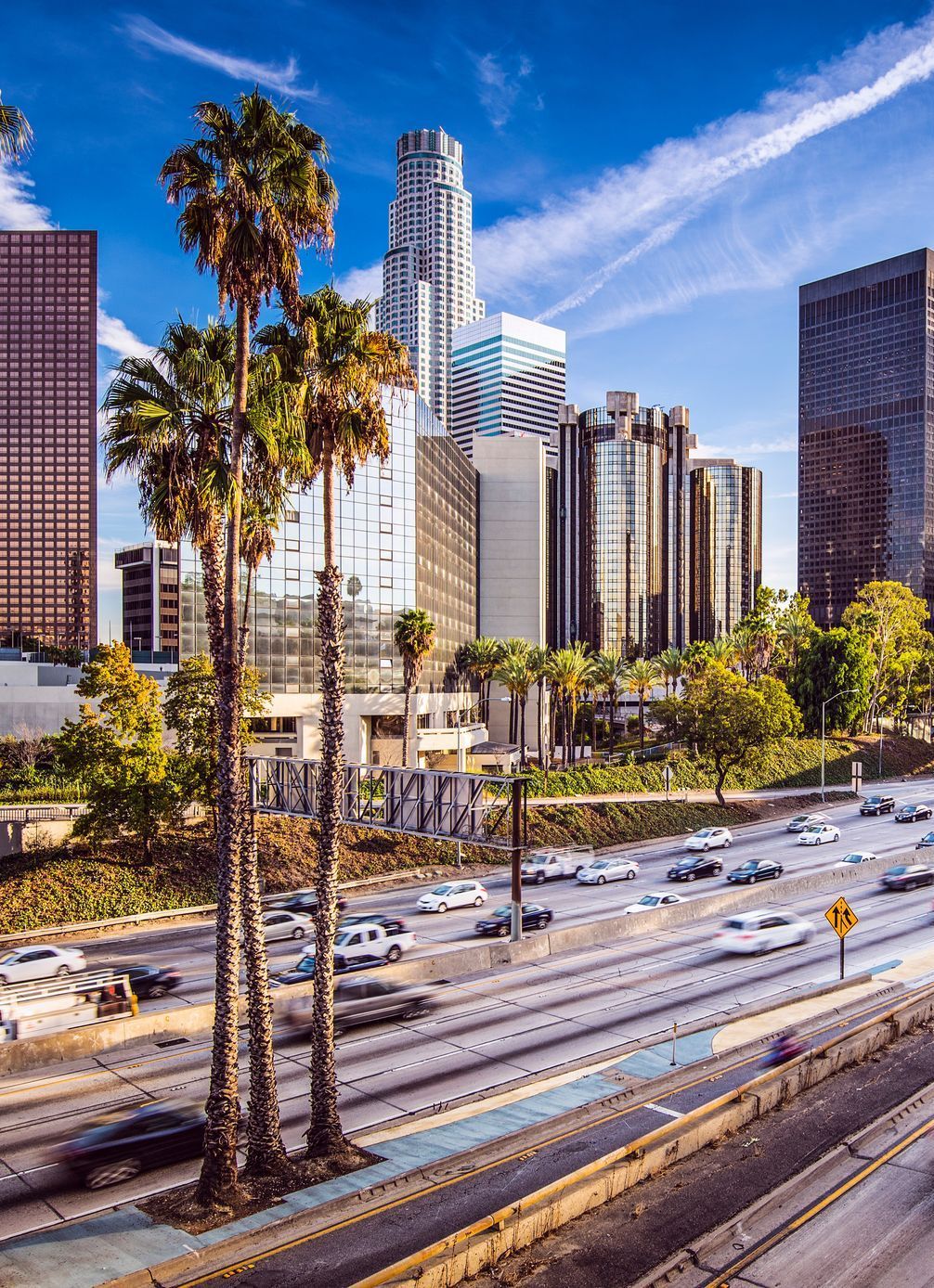 An aerial view of a city with a highway and palm trees in the foreground.