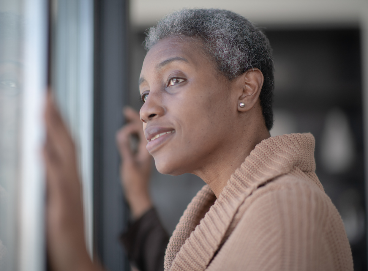 Woman with short gray hair looks out a window, wearing a tan sweater.