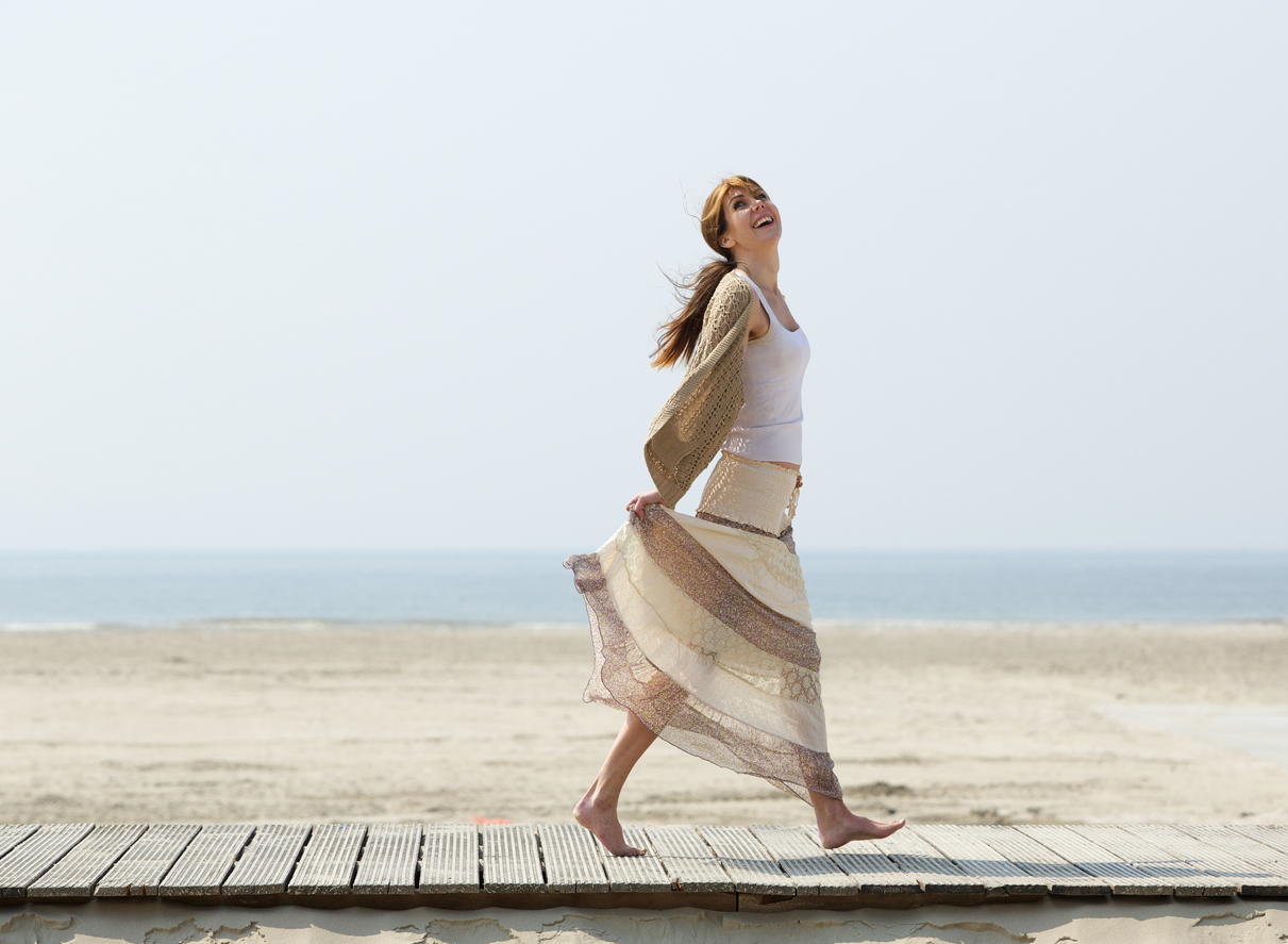 Woman walking barefoot on wooden planks at the beach, smiling.
