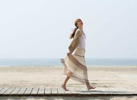 Woman walking barefoot on wooden planks at the beach, smiling.
