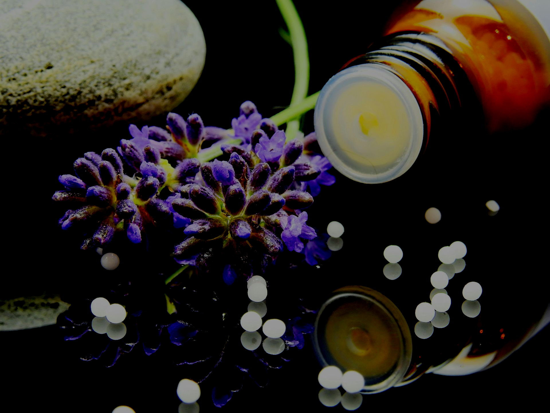 Lavender, homeopathy bottle, white pills, and stone on a reflective black surface.
