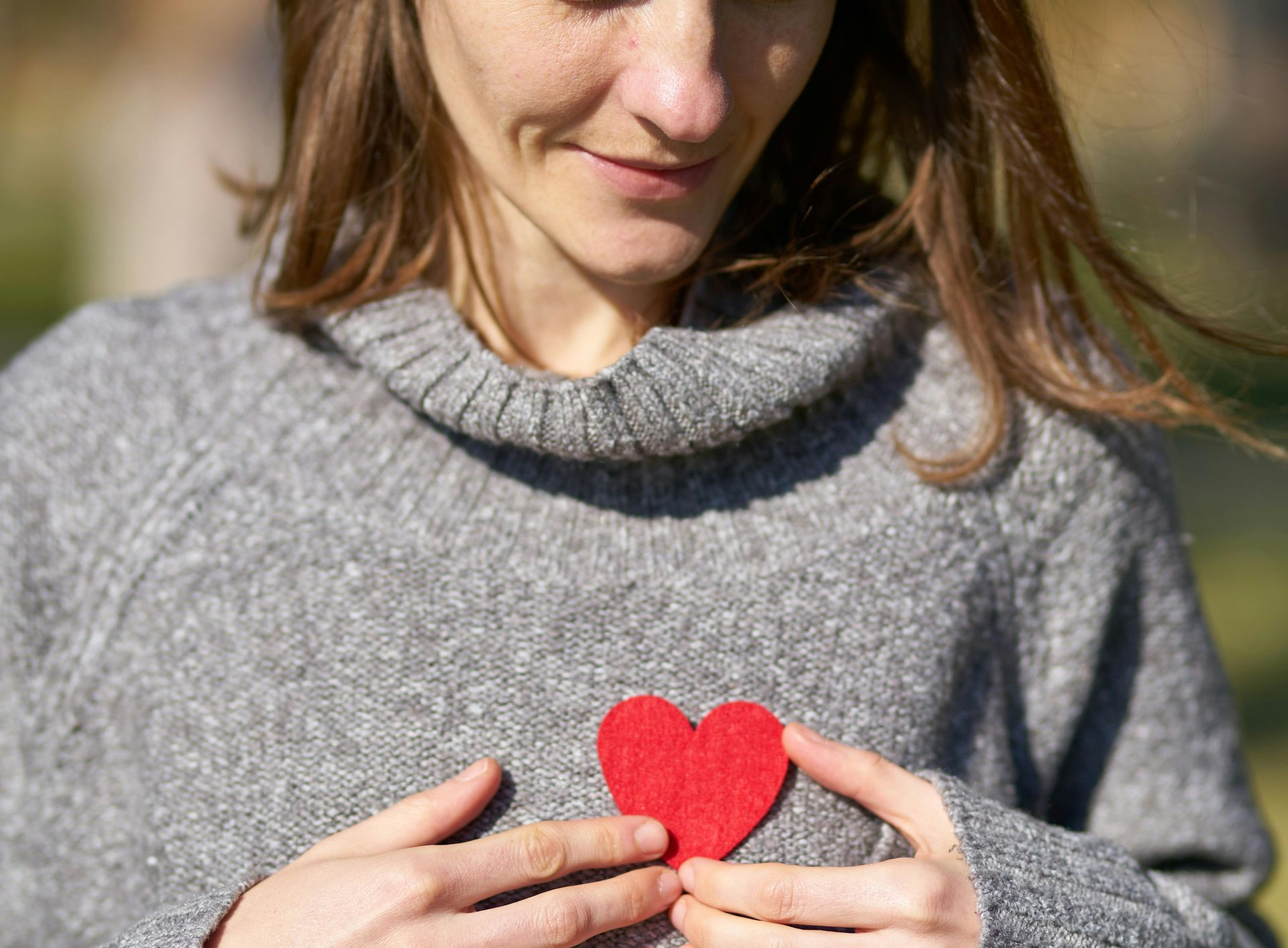 Woman holding a red felt heart over her chest, smiling.