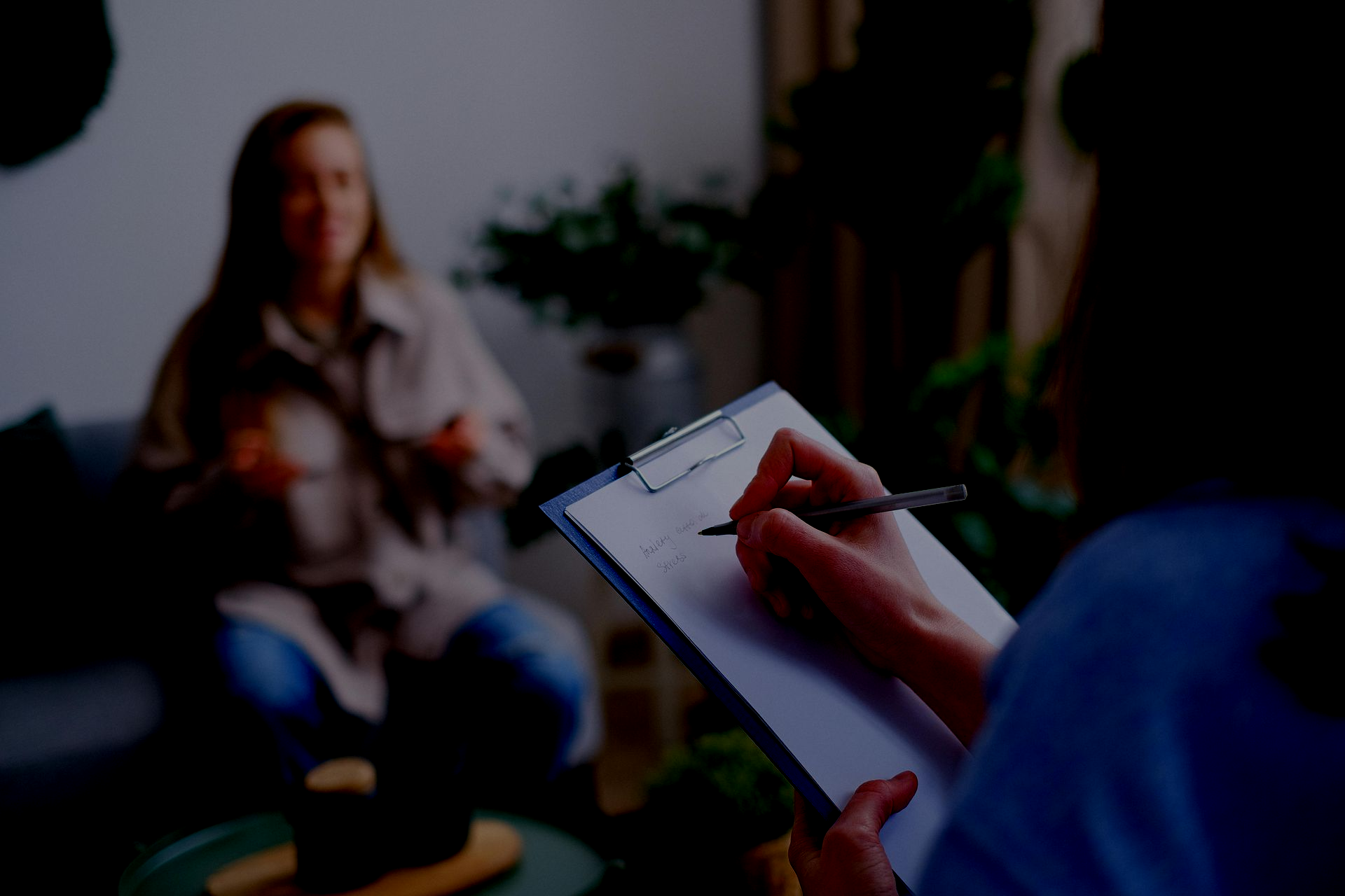 Person taking notes on clipboard during therapy session.