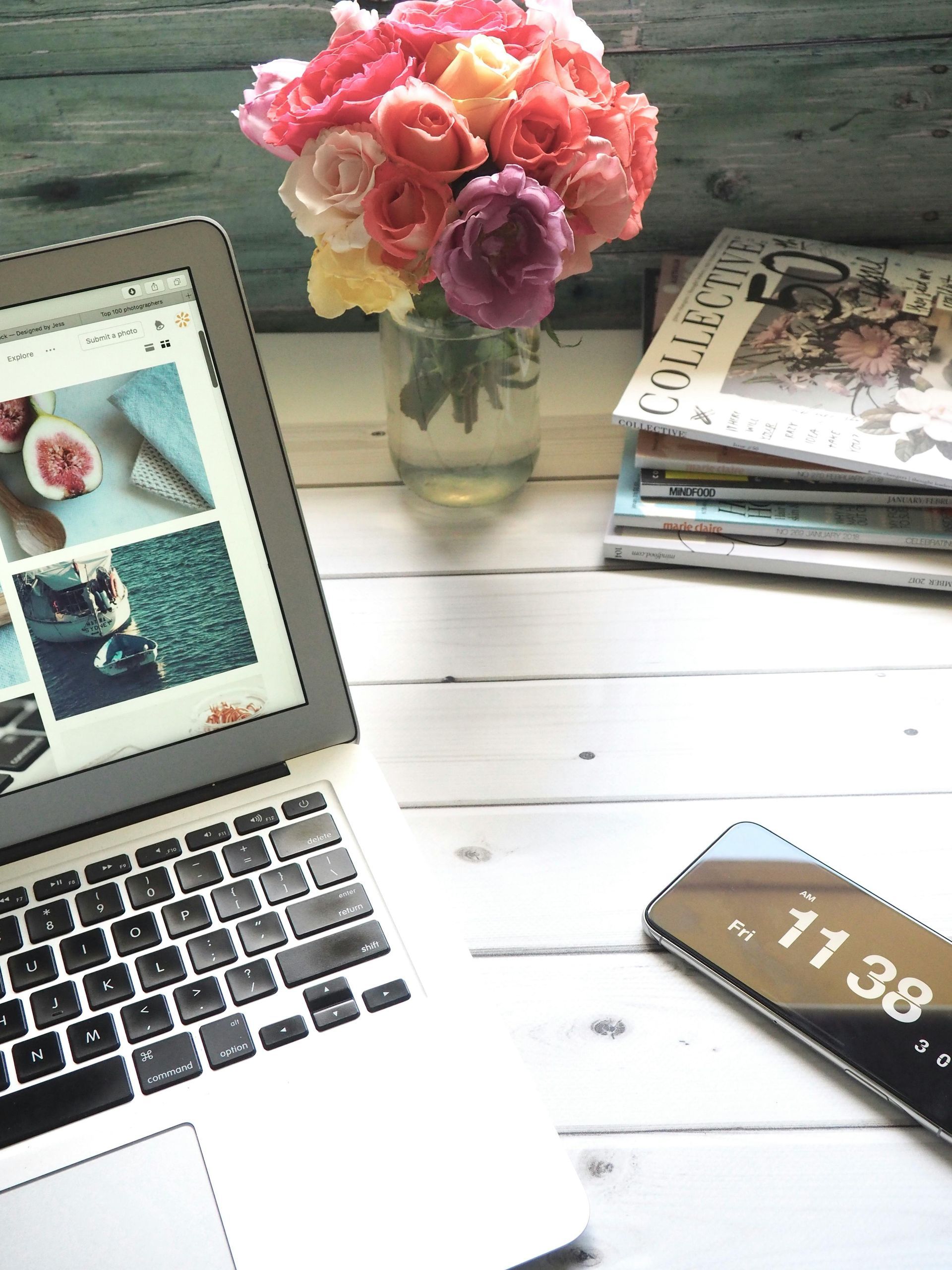 Laptop, phone, and flowers on a white desk. Laptop displays a website, roses in a vase.