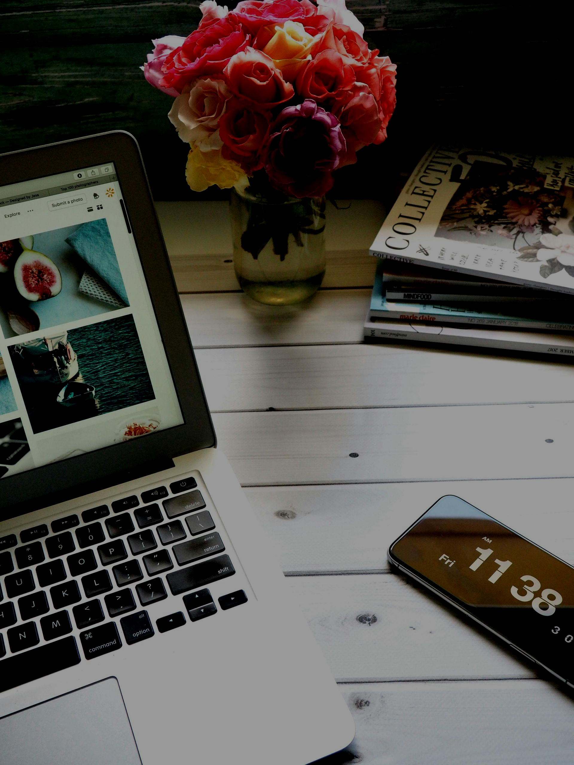 Laptop with website open, beside a digital clock and flowers on a white wooden surface.