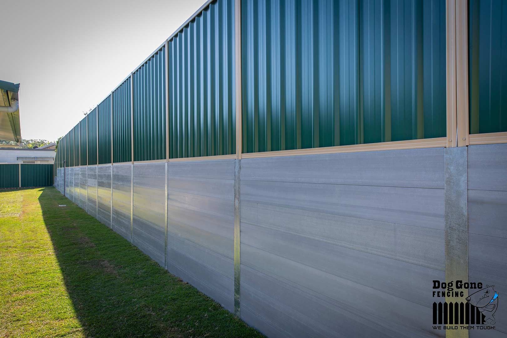 A Green Colorbond Fence Is Sitting At The Top Of A Retaining Wall — Dog Gone Fencing in Brisbane, QLD